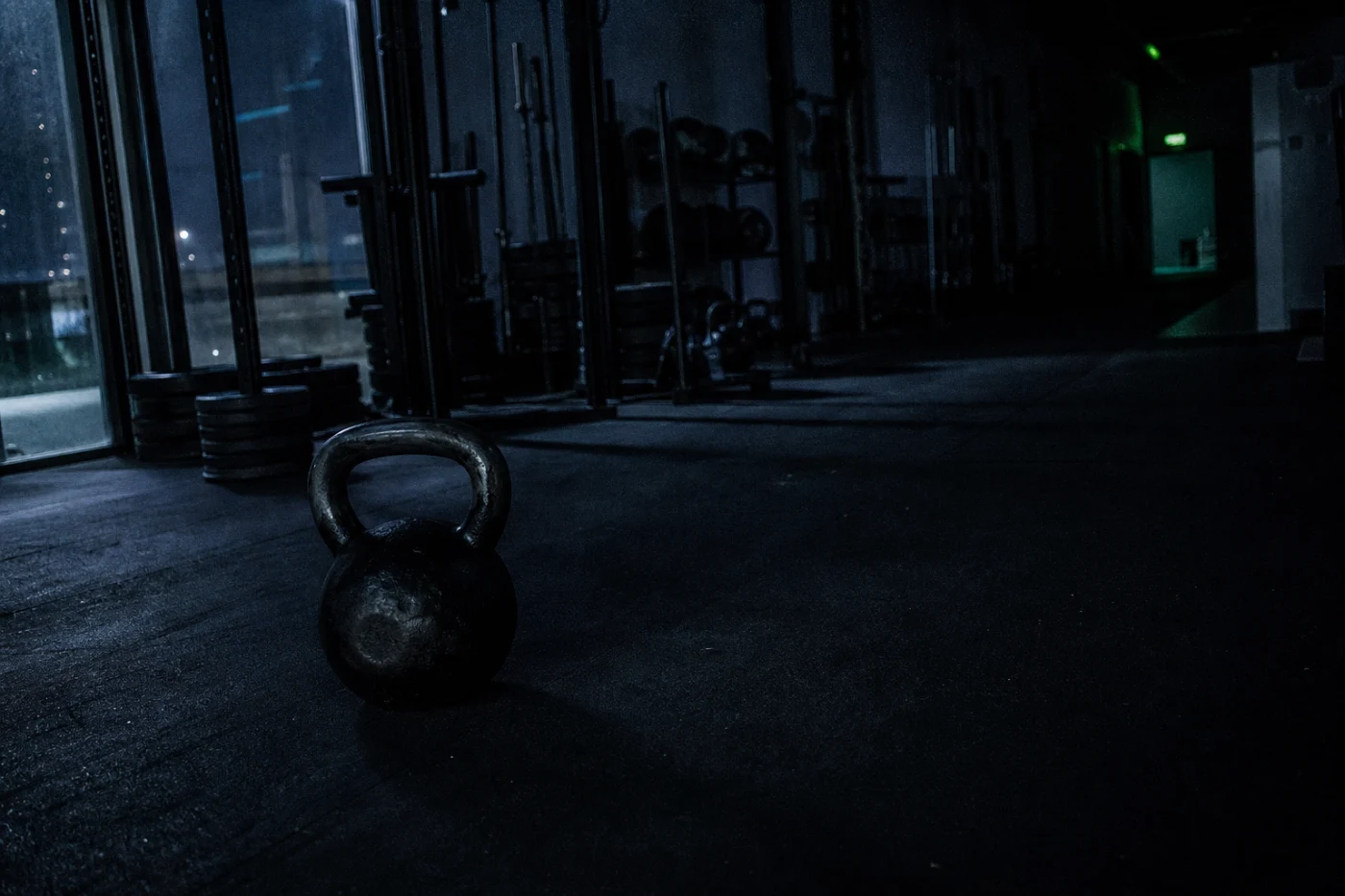 An independent gym after closing, equipment racked and still, lit only by a streetlight through the glazed frontage.