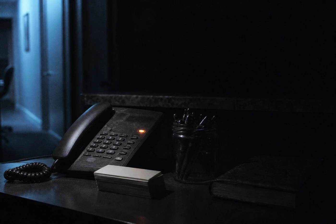 A clinic reception counter after hours, the desk phone showing a message-waiting light in near darkness.