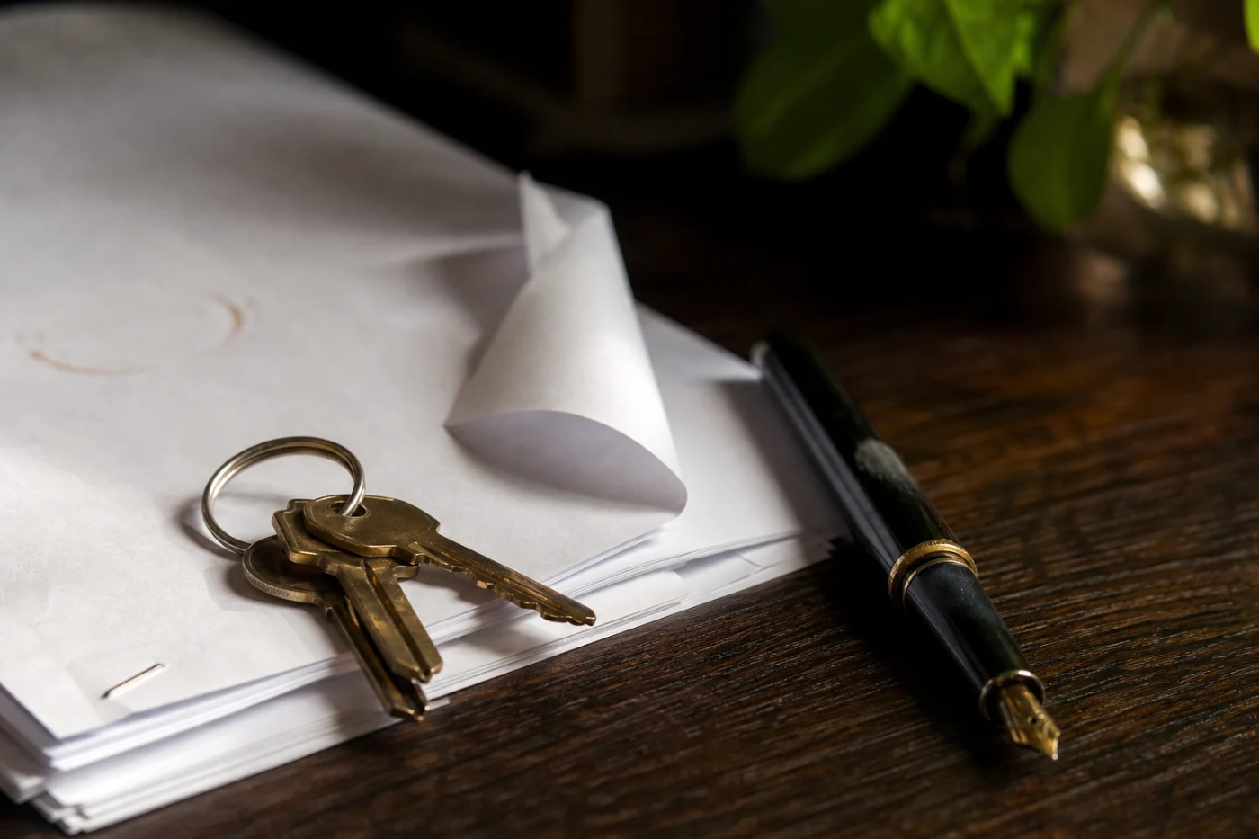 House keys resting on a stack of printed contract pages with a fountain pen laid diagonally beside them.